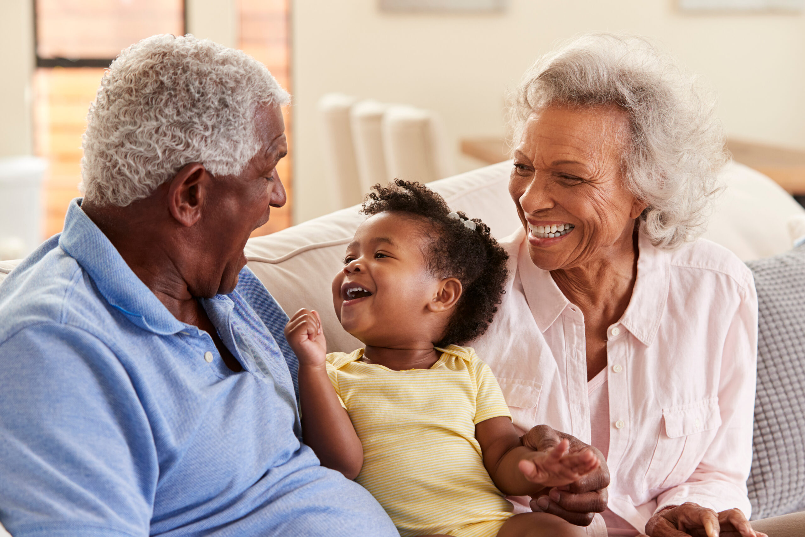 Grandparents,Sitting,On,Sofa,At,Home,Playing,With,Baby,Granddaughter